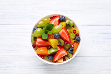 Delicious fresh fruit salad in bowl on white wooden table, top view
