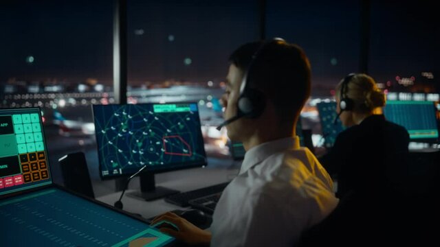 Male Air Traffic Controller with Headset Talk on a Call in Airport Tower. Office Room is Full of Desktop Computer Displays with Navigation Screens, Airplane Departure and Arrival Data for the Team.