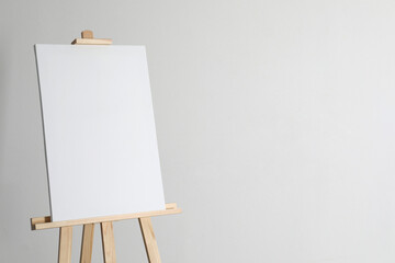 Wooden easel with blank canvas on light background. Space for text