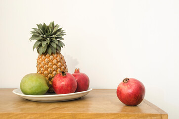 Pineapple, pomegranate and mango in a saucer on a wooden table