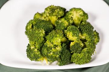 healthy food, boiled broccoli on a white plate on a dark green cloth