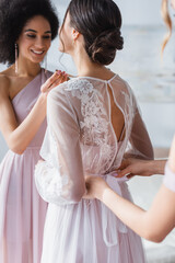 african american woman with friend preparing bride for wedding, blurred foreground.