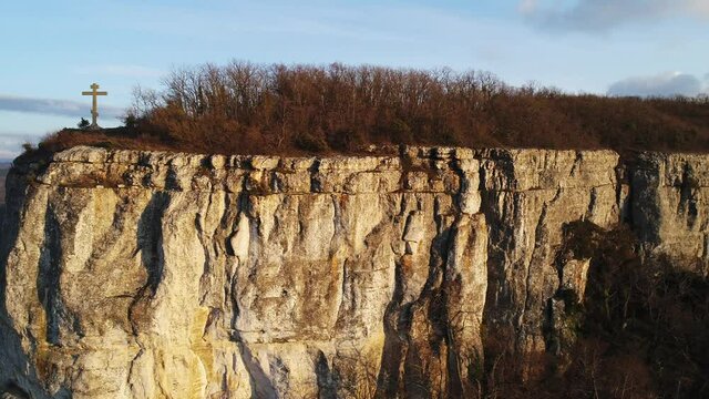 Panoramic landscape with rock cliff and christian cross on its peak. Shot. Concept of religion, place of faith and peace, aerial view of a mountain and and a cross.
