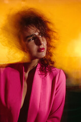 A beautiful well-groomed girl in a crimson jacket of multicolored flying fabric is sitting on a chair.