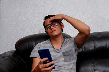 Young Latino in his twenties receiving bad news on his smartphone sitting on his sofa