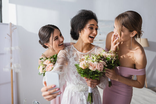 laughing african american bride taking selfie with cheerful friends, blurred foreground.
