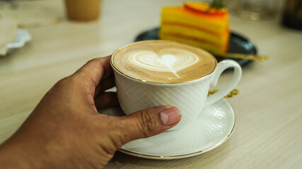 A man hand holding Hot Latte art cup of coffee on wooden table