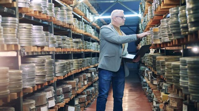 Archive specialist with a laptop is observing cases with film tape