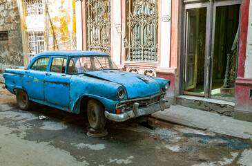 A dilapidated light blue car parked on a residential Havana street with its front end raised up by...