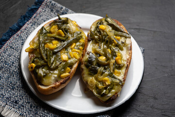 Molletes with poblano rajas and cheese on dark background. Mexican food