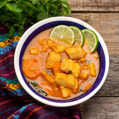 Fish soup with vegetables on wooden background. Mexican food