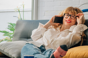 Obraz premium smiling woman with mobile phone on the sofa at home