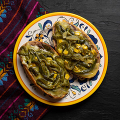 Molletes with poblano rajas and cheese on dark background. Mexican food