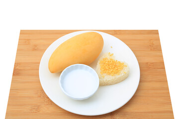 Golden mango and sticky rice served with coconut cream on white circle ceramic plate on bamboo board background. Tropical summer fruit in thailand