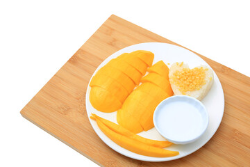 Golden mango and sticky rice served with coconut cream on white circle ceramic plate on bamboo board background. Tropical summer fruit in thailand