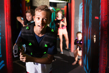 Obraz na płótnie Canvas Emotional teen boy with laser pistol playing laser tag with friends on dark labyrinth..