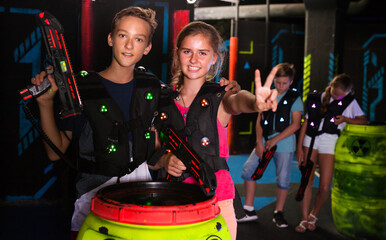 Fototapeta na wymiar Cheerful teen girl and boy with laser pistols posing together in laser tag labyrinth..