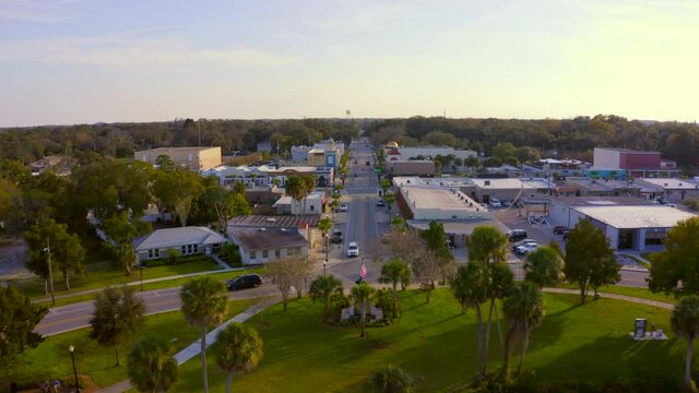 Backwards Aerial Pan From Main Road of a Small Town to Trees Reflecting on Pond