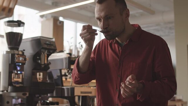 Tilt up of professional male barista standing at worktop in bar and tasting different types of coffee in cup tasters. Coffee degustation