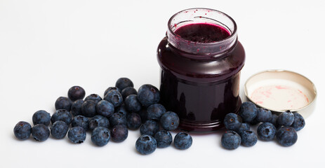 Healthy vitamin food. Ripe berries of fresh sweet bilberries and jar of blueberry jam on white background