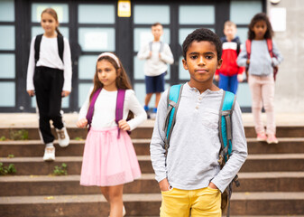 Portrait of african american boy standing near school, children on background