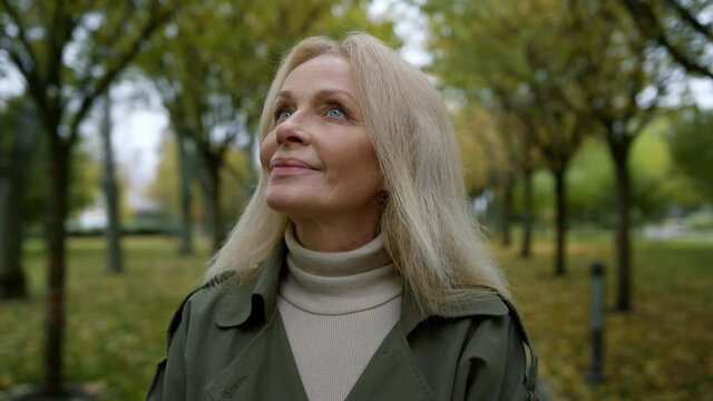 Portrait of romantic woman looking into sky through trees branches in park .