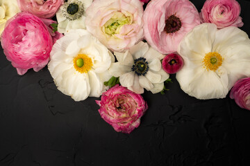 Fresh ranunculus and anemone floral flat lay on black textured background