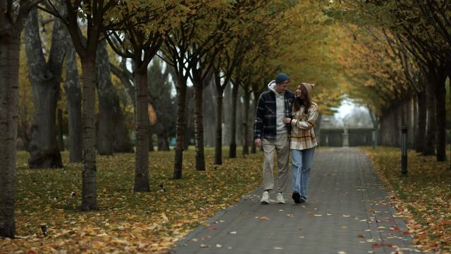 Cheerful lovers walking happily along alley in foliage park. Beautiful couple.