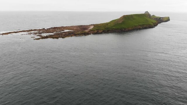 Smooth Revealing Drone Shot of Worms Head, Rhossili Bay and Rhossili Beach in The Gower Peninsula, Wales. Showing Crashing Waves Hitting off The Rocks and Worms Head in The Distance.