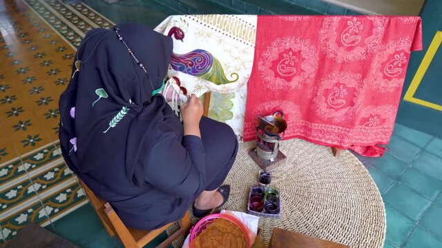 Rear view of Muslim woman creating unique batik motif on fabric using melted wax