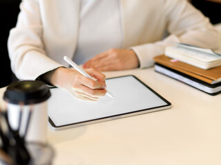 Close up view of female hand working on digital tablet with stylus pen on white desk with stationery