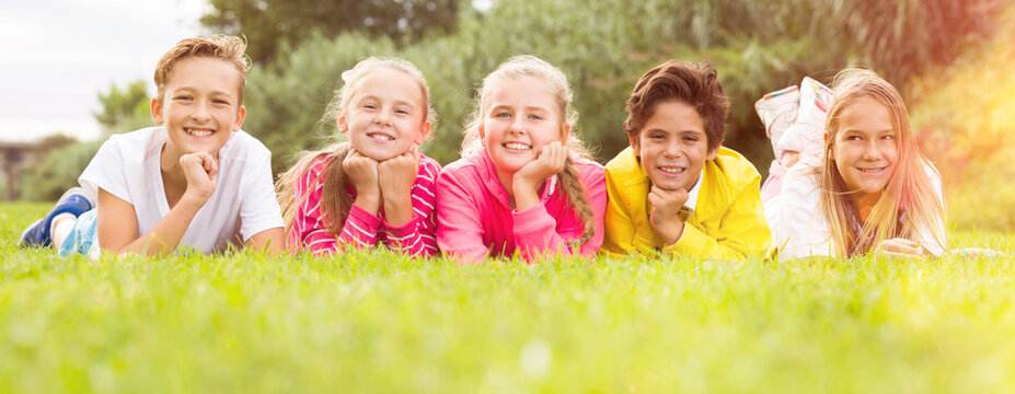 Portrait of five kids who are walking and posing lying in the park.