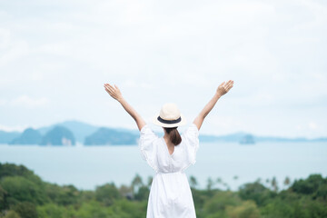 Happy traveler woman in white dress enjoy Beautiful view, alone Tourist with hat standing and relaxing over ocean. travel, summer and vacation concept