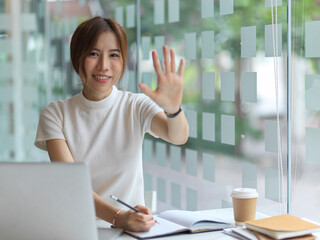 Portrait of female smiling and shoeing five palm leave hand to camera while working in workplace