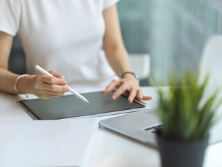 Female student hands using digital tablet to do homework on white desk in library
