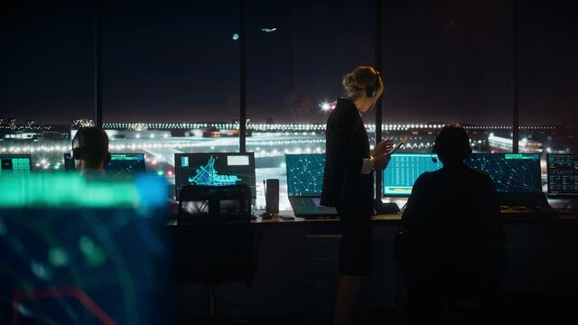 Female and Male Air Traffic Controllers with Headsets Talk in Airport Tower at Night. Office Room Full of Desktop Computer Displays with Navigation Screens, Airplane Flight Radar Data for Controllers.