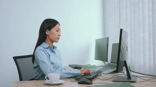 Asian woman is sitting in the office while checking the information to match the documents.