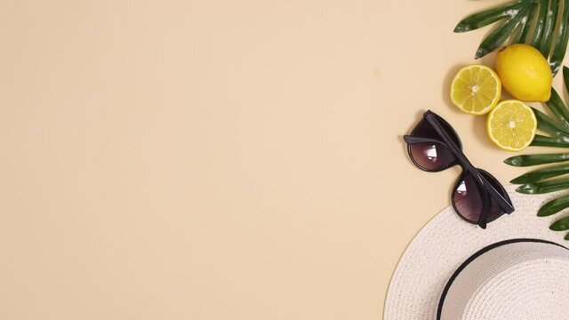 Summer hat and sunglasses move with tropic palm laves and lemons on sandy background. Stop motion flay lay