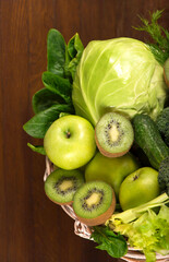 Green vegetables - kiwi, cabbage, herbs, celery, broccoli, cucumbers in a basket a wooden background