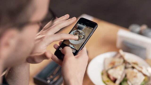 Close-up of male hands holding smartphone and taking pictures of food on table in restaurant