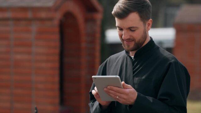 Cute male monk in a black robe on the street with a laptop