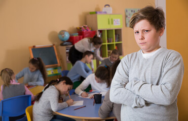 Fototapeta na wymiar Portrait of sadly schoolboy and children drawing in classroom