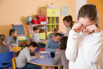 Portrait of sad ordinary schoolgirl and children drawing in classroom