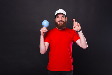 I wish to travel the world, happy bearded hipster man crossing fingers and holding globe