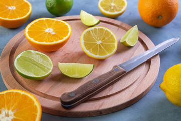 Close-up of a kitchen knife and ripe citrus fruits whole and cut on a round wooden cutting board. Selective focus.