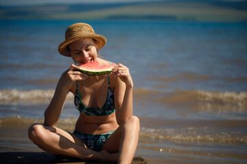 Fototapeta premium Portrait of smiling woman relaxing holding and eating a slice of watermelon on the tropical beach