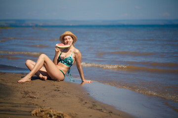 Fototapeta premium Portrait of smiling woman relaxing holding and eating a slice of watermelon on the tropical beach