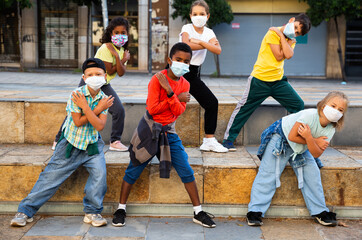 Preteen boys and girls breakdancers in medical masks dancing on city street in summer. Concept of precautions during coronavirus pandemic.