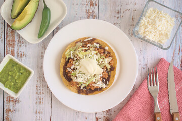 Traditional Mexican food. Picadillo toast with guacamole, sour cream, lettuce and cheese, accompanied by avocado slices and jalapeño peppers.