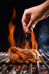 Hand sprinkling salt and spices on grilled chicken leg on the flaming grill © amenic181
